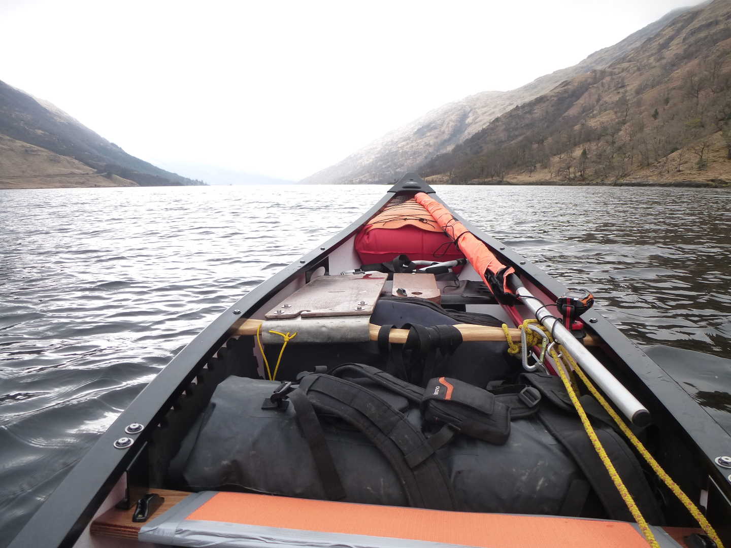 View of a loch from inside a kayak. The front of the kayak filled with equipment can be seen