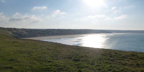 A view of a beach from the clifftops with the sun in the distance