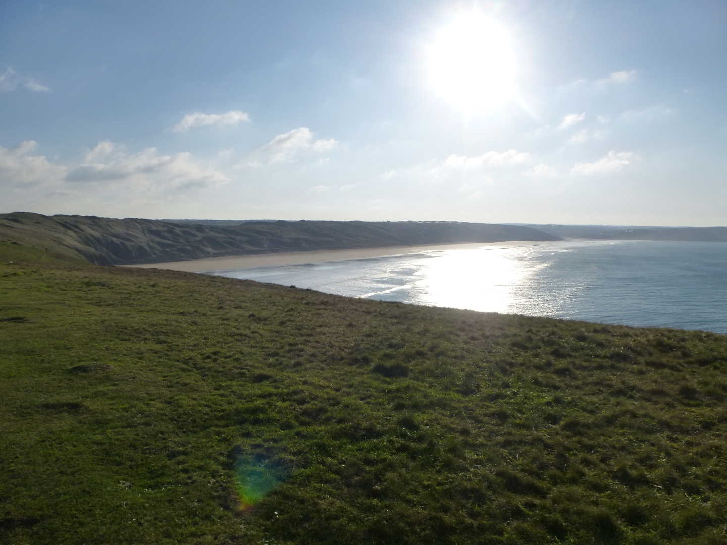 A view of the beach from the clifftops with the sun in the distance